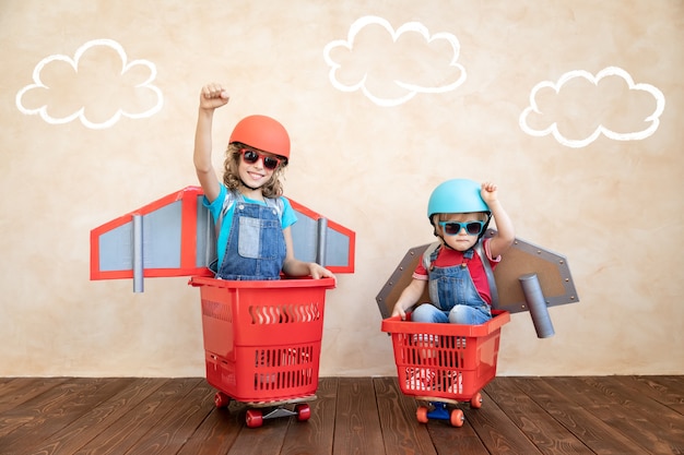 Photo kids with paper rocket racing on shopping cart indoor