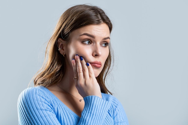 Kiespijn Vrouw met tandinfectie Vrouw lijdt aan kiespijn tegen een grijze achtergrond Jonge vrouw lijdt aan kiespijn Meisje lijdt aan kiespijn, tandbederf of gevoeligheid