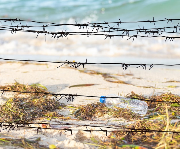 Kijk door het prikkeldraad op een vies strand vol zeewierafval en lege plastic fles