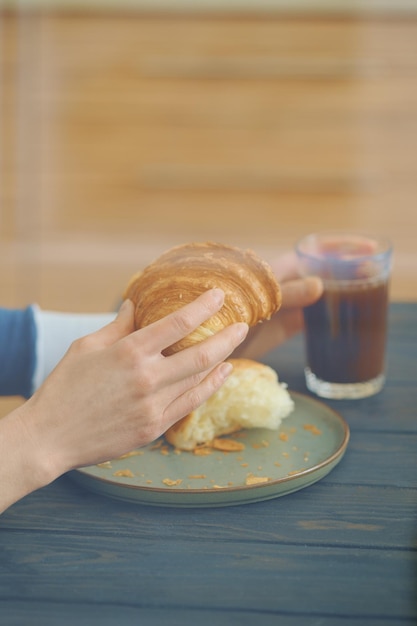 Kijk door het raam op handen van vrouw met croissant