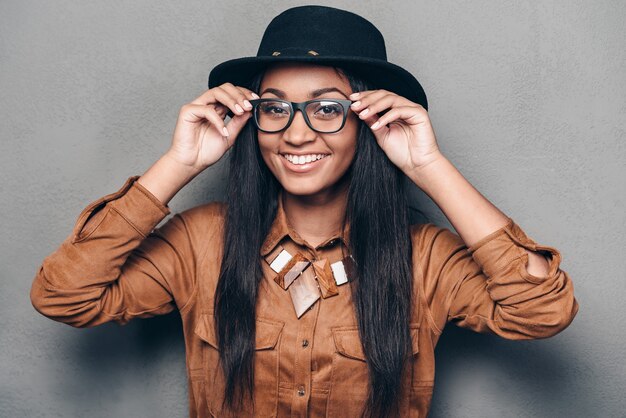 Kijk eens van dichterbij! Portret van mooie jonge Afrikaanse vrouw die haar bril aanpast en met een glimlach