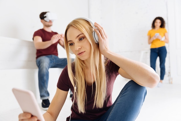 Kijk gewoon. Attente vrouwelijke persoon koptelefoon aan te raken en het hoofd te buigen terwijl ze naar haar telefoon kijkt