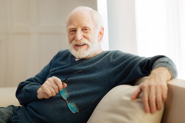 Kijk naar me. Knappe mannelijke persoon die glimlach op zijn gezicht houdt en glazen houdt