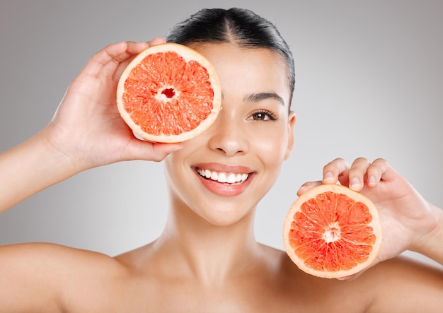 Kijk wat ik zie Heel veel vitamine C Studio-opname van een aantrekkelijke jonge vrouw die grapefruit tegen haar gezicht houdt tegen een grijze achtergrond