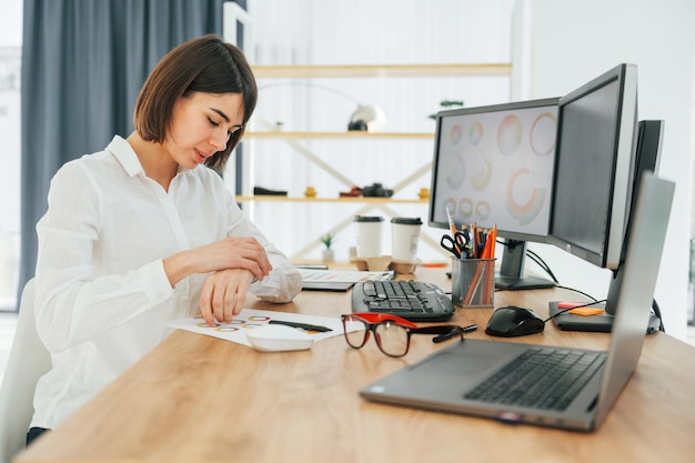 Kijken naar horloges Vrouwelijke ontwerper die op kantoor werkt met behulp van pc