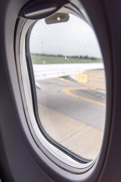 Foto kijkend door het raam van het vliegtuig dat zich tijdens het regenen op de baan beweegt