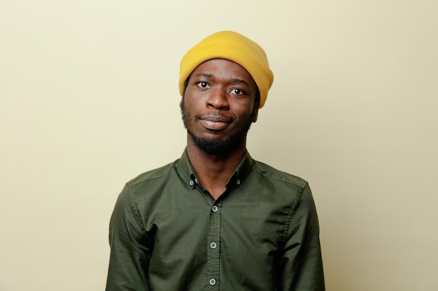 Kijkend naar camera jonge Afro-Amerikaanse man in hoed met groen shirt geïsoleerd op een witte achtergrond