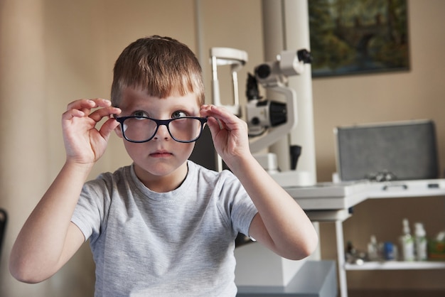 Kijkend naar de zijkant. Portret van een kind zittend met een bril in de kliniek van de arts met oftalmische apparatuur