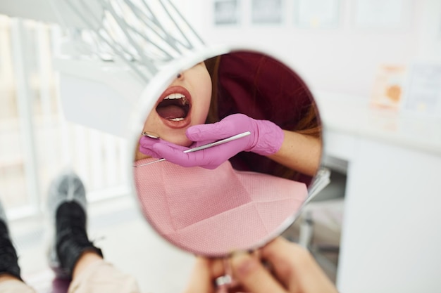 Kijkt naar spiegel Meisje op bezoek bij tandarts in kliniek Conceptie van stomatologie