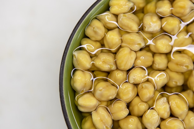 Kikkererwten gedrenkt in water, in kom, op marmeren tafel. Concept van gezond eten, veganisme, vegetarisme, vlees- en eiervervanging. Bereid kikkererwten voor voordat u hummus en andere peulvruchtengerechten maakt.