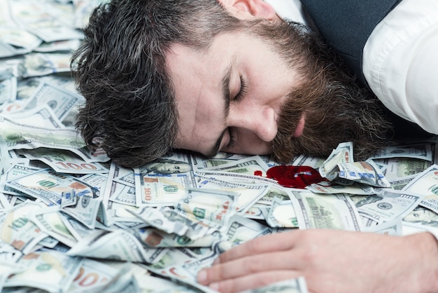 Killed by money. Business man, millionaire, billionaire, bearded man lying in banknotes. Portrait of killed bearded man lying in money.