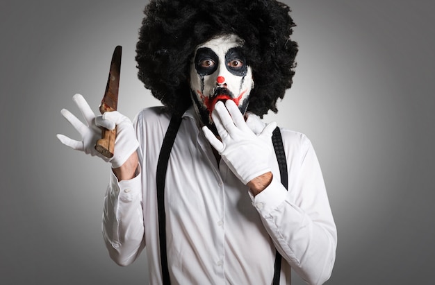 Photo killer clown with knife making surprise gesture on textured back