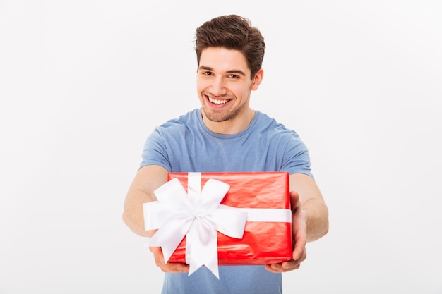 Kind attractive man with beautiful smile giving birthday present on camera, isolated over white wall