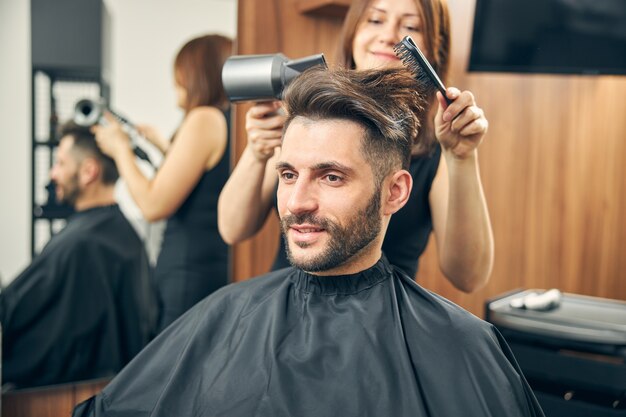 Kind bearded male person keeping smile on his face listening to his stylist