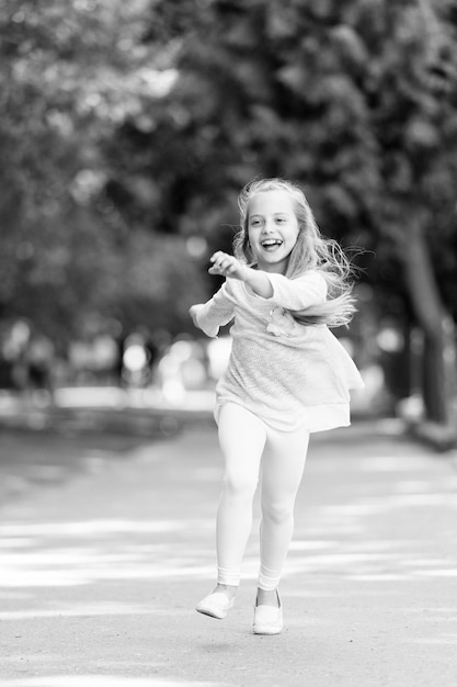 Kind blij en vrolijk geniet van wandeling in het park Jeugdconcept Kid meisje met vrolijke uitdrukking rennen of lopen op internationale kinderdag Meisje op blij lachend gezicht wandelingen natuur op achtergrond