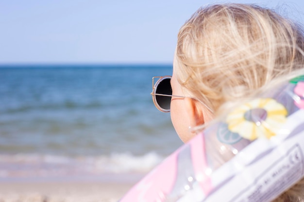 Kind blond meisje in zonnebril met een rubberen ring op het strand