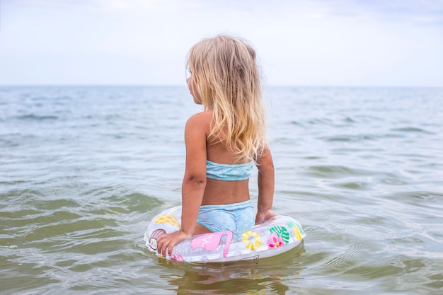 Kind blond meisje met een opblaasbare ring baadt in de zee