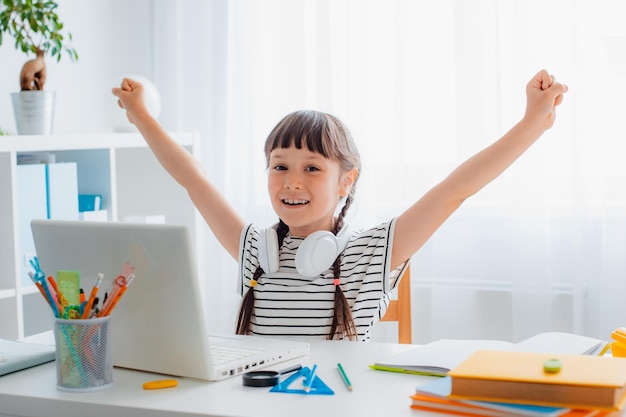 Kind brunette schoolmeisje huiswerk tijdens een online les thuis in een helderwitte kamer s