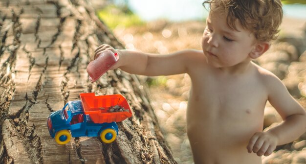 Kind buiten spelen. Kid we gieten het zand in de rode vrachtwagen. Kinderen straatspellen. Een jongen die met een machine op het grote blok speelt