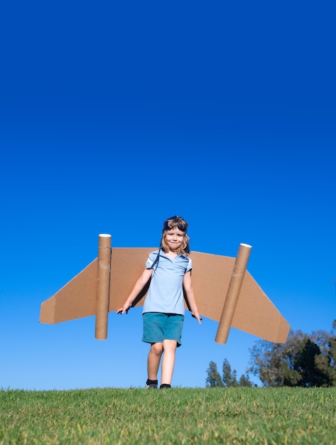 Foto kind buiten spelen op groen gras en blauwe lucht kid piloot met speelgoed jetpack kid jongen spelen met speelgoed p