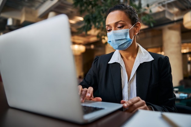 Kind dark-skinned woman sitting at the table in cafe and checking her mailbox online while waiting for coffee