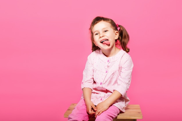 Kind dat de aap speelt. Weinig babymeisje dat roze kleren draagt tegen een roze