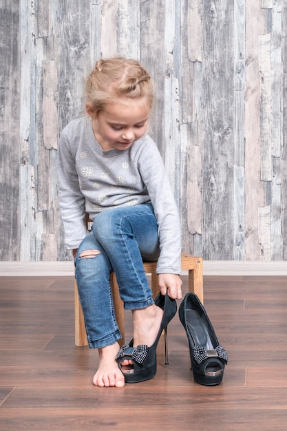 kind draagt haar moederschoenen aan het been terwijl ze op een kleine houten stoel zit