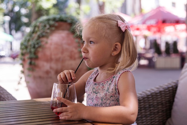 Kind drinkt een drankje op het zomerterras onder natuurlijk licht. echte mensen.