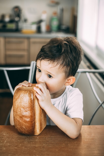 kind eet overdag aan tafel gretig een heel brood in de vorm van een baksteen