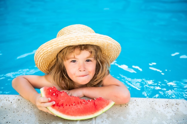 Kind eet watermeloen in het zwembad Leuke jongen die een plakje rode watermeloen eet op het strand Gelukkige kaukasische jongenswatermeloen tegen het blauwe water