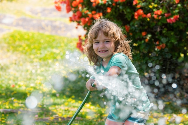 Kind geeft bloemen en planten water in de tuin Kind met waterslang in de achtertuin Kinderen Tuinieren Kinderen summ