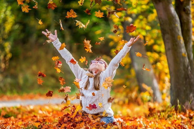 Kind gooit in de herfst graag oranje bladeren boven haar.