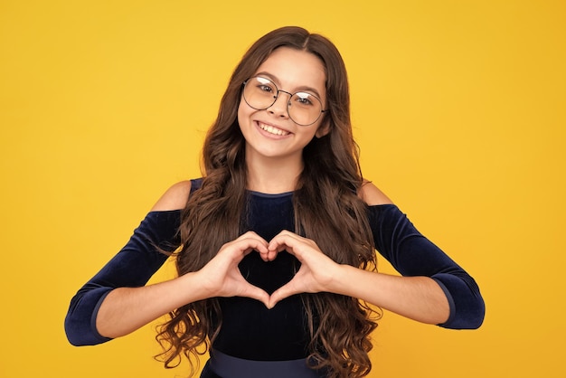 Kind handen maken teken hart door vingers Mooie romantische tienermeisje houdt rood hart symbool van liefde voor Valentijnsdag geïsoleerd op gele achtergrond