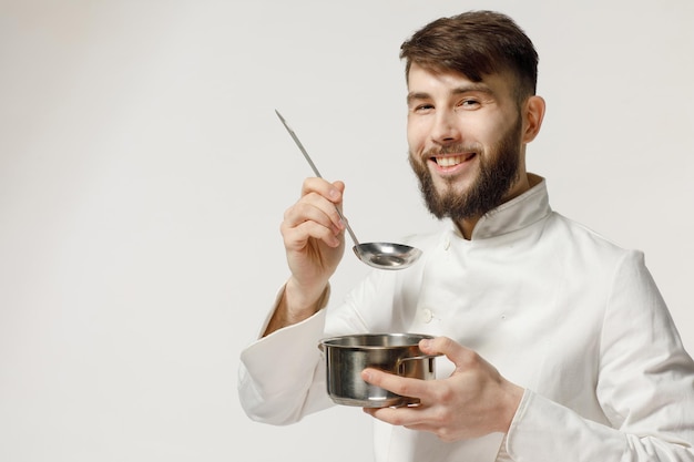 Il cuoco gentile e bello tiene gli utensili da cucina su un concetto di fondo bianco isolato per un cuoco