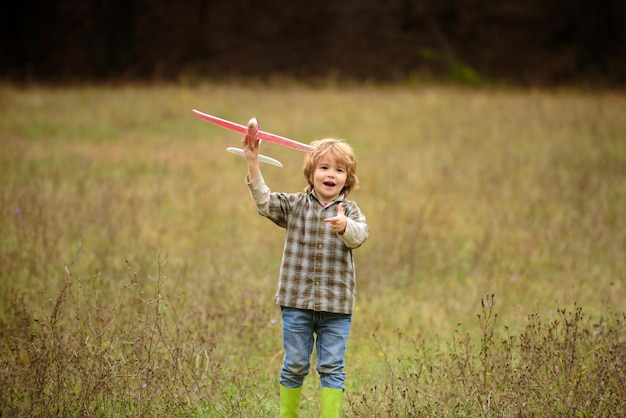 Kind heeft plezier met speelgoedvliegtuig in het veld kleine jongen met houten vliegtuigjongen wil piloot worden en