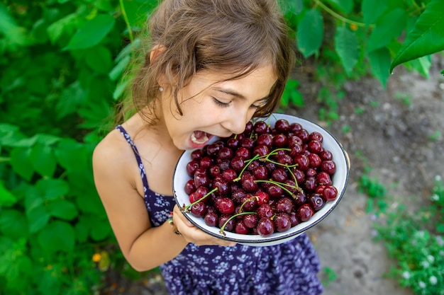 Kind houdt een kom met kersen op tuinachtergrond