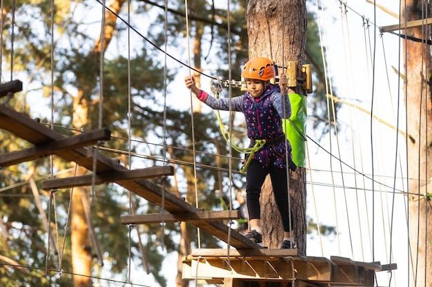 Kind in bos avonturenpark. Kinderen klimmen op een hoog touwpad. Behendigheid en klimmen outdoor amusement centrum voor kinderen. Klein meisje buiten spelen. Schoolpleinspeeltuin met touwbaan.