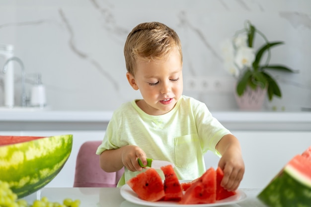 kind in de keuken van het huis een baby eet een watermeloen lacht het concept van gezond eten