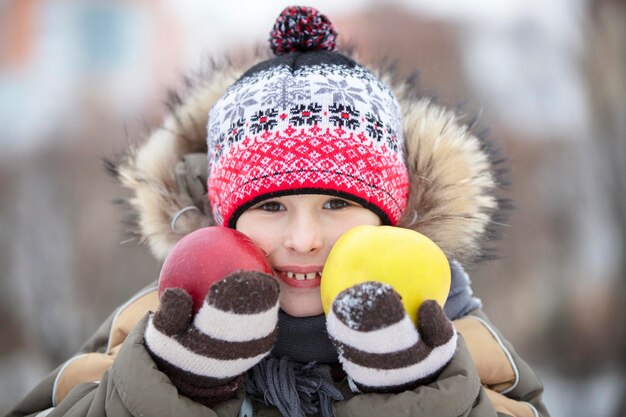 Kind in de winter met fruit De jongen met de hoed houdt twee grote appels vast
