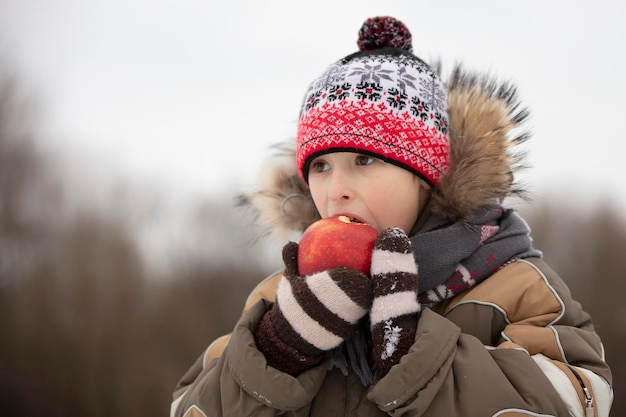 Kind in de winter met fruit Jongen die een rode appel eet