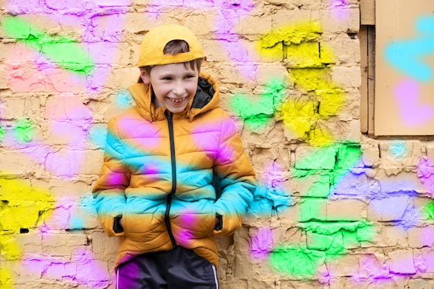 Kind in graffiti De jongen staat in modieuze kleding tegen een bakstenen muur