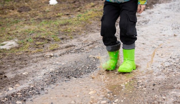 kind in groene rubberen laarzen rennen op stroom lente