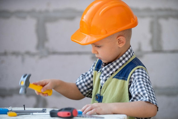 Kind in harde hoed met hamer Klein kind helpt met speelgoedgereedschap op bouwplaats Kinderen met bouwgereedschap Kinderen bouwer en reparatie bouwvakker