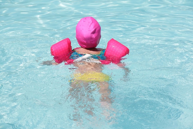 Kind in het zwembad zwemmen met roze vlotter met blauw water