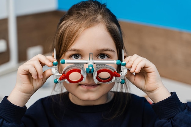 Kind in proefmontuurbril op blauwe achtergrond Onderzoek met kinderoogarts voor selectie van proefbrilmontuur om het visuele oogsysteem te onderzoeken