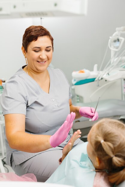 Kind is blij na tandheelkundige behandeling en geeft high-five aan zijn arts in een moderne witte tandheelkundige kliniek.