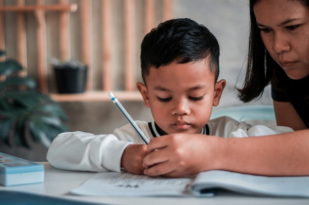 Kind jongen bedrijf potlood schrijven. Aziatische jongen doet huiswerk, schrijfpapier voor kinderen, onderwijsconcept, terug naar school.