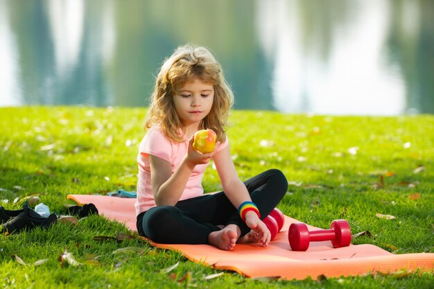 Kind jongen eet appel ontspannen op sportmat na sportoefeningen buiten in het park