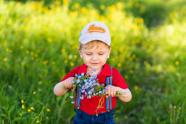 Kind jongen heeft plezier met spelen in de natuur tussen bloemen en verzamelt een boeket