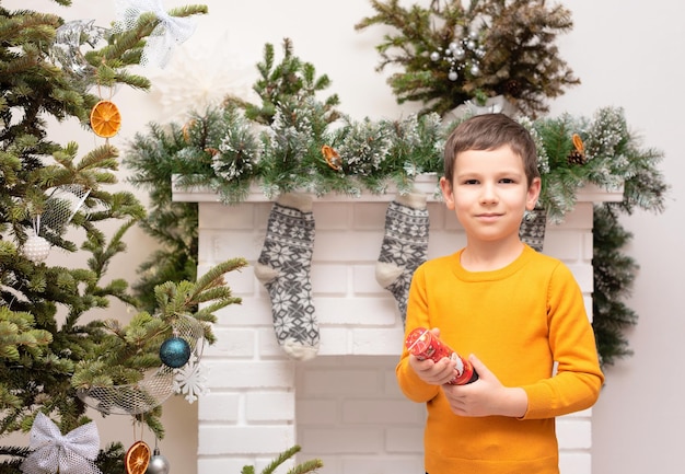 Kind jongen met petard in zijn handen in de buurt van versierde kerstboom en open haard winter of nieuwjaar gezellige vakantie concept xmas achtergrond met selectieve focus